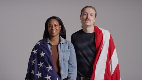 retrato de estudio de una pareja multicultural envuelta en la bandera estadounidense detrás de ellos celebrando el 4 de julio, día de la independencia