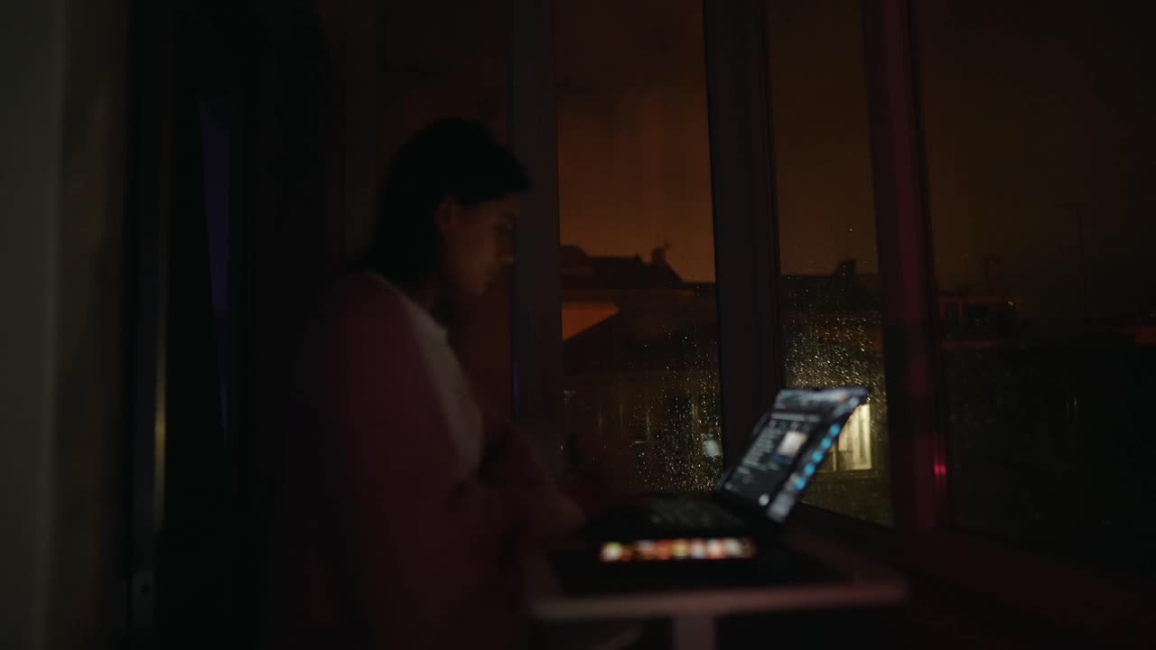 Donna che usa un portatile di notte vicino alla finestra