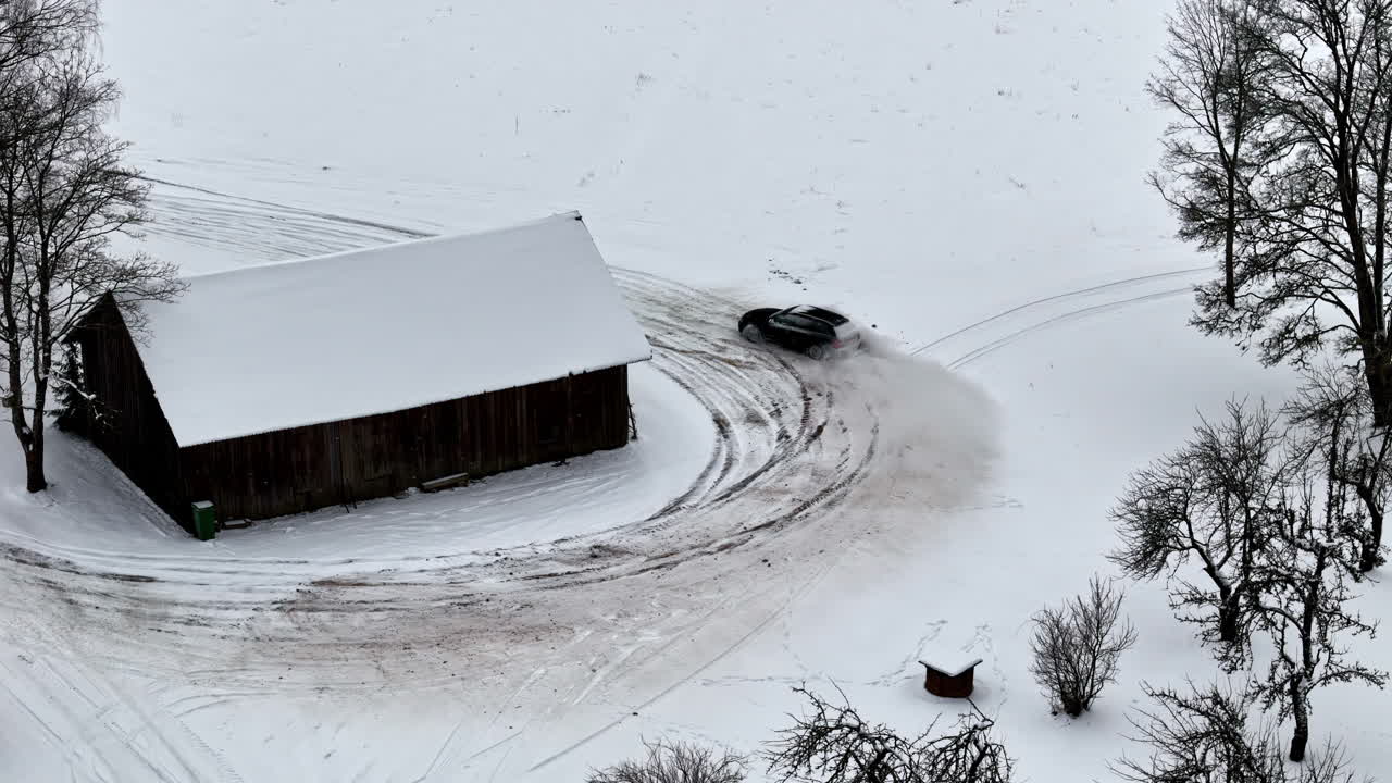 A Car is Drifting Around a Snowy Barn, Leaving Curved Tire Tracks on the Snow-covered Ground - High Angle Shot