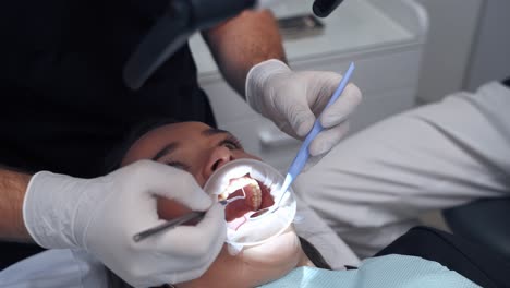 close-up woman's face with opened mouth at dentist. doctor hands in gloves examines patient's teeth by medical tools. dentistry concept.