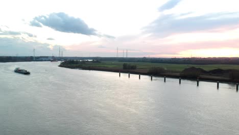 Drohne,-Die-Sich-Bei-Sonnenuntergang-Mit-Einem-Frachtschiff-über-Den-Fluss-Senkt