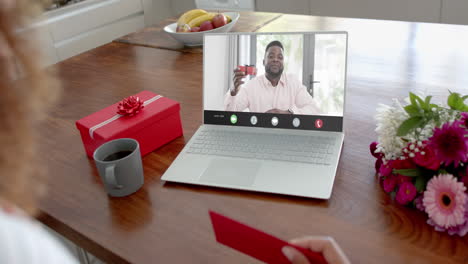 Caucasian-woman-holding-envelope-and-talking-with-african-american-man-on-laptop-screen