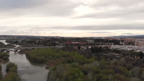 Drone-En-Aumento-Sobre-El-Río-Y-El-área-Industrial-Con-Parque-En-Un-Día-Nublado