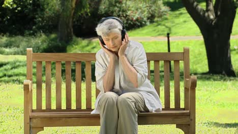 Old-woman-listening-to-music-with-headset-on-a-bench