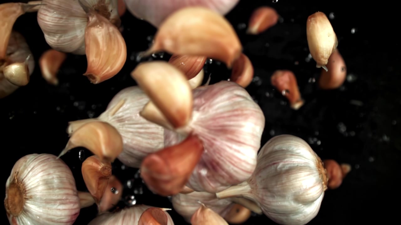 Bulbi e spicchi d'aglio freschi che cadono al rallentatore con goccioline d'acqua