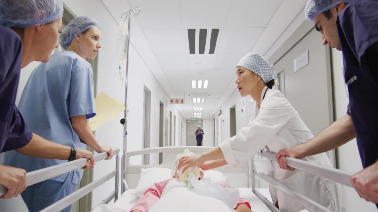Video di un gruppo eterogeneo di operatori sanitari che spostano un paziente con ventilatore su un letto lungo il corridoio dell'ospedale.