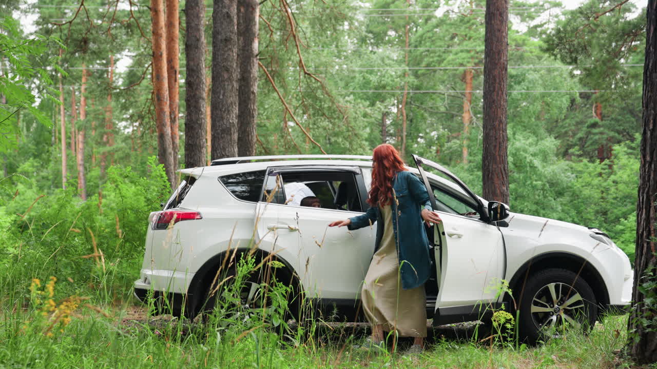 White family vehicle parked in arboretum amid autumn trees, mother steps out while husband sits in front, kids visible inside, peaceful stop in forest clearing before walk, doors open, soft daylight