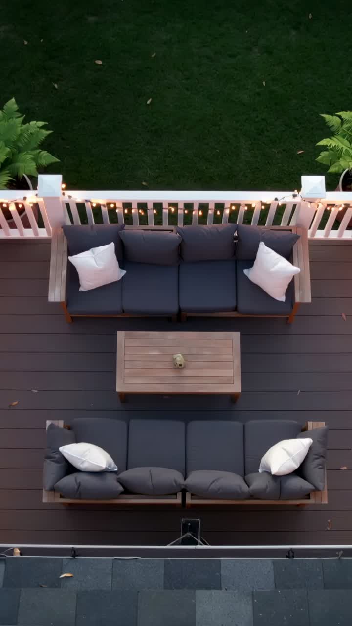 Vertical video: Shifting overhead view showing gray sofas with wooden table on deck, capturing dusk