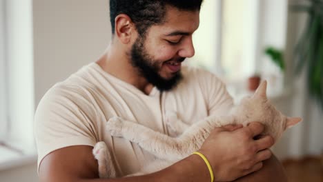 Bearded-young-man-holds-a-peach-color-cat-in-his-arms-and-caress-him