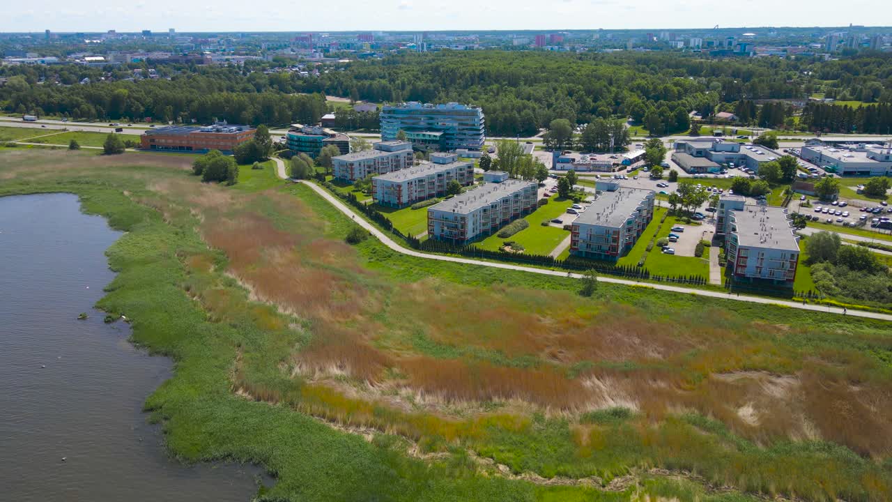 Aerial drone video moving sideways and revealing a large urban shoreline area in Rocca al Mare during a sunny day at summer. Houses are built near Baltic sea water and beach grass is visible below.