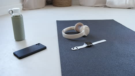 yoga mat with smartwatch, headphones, smartphone, and water bottle in workout space, at home