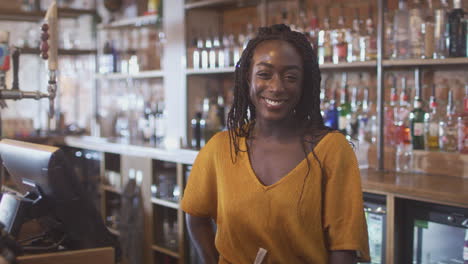 portrait of smiling female bar worker standing behind counter