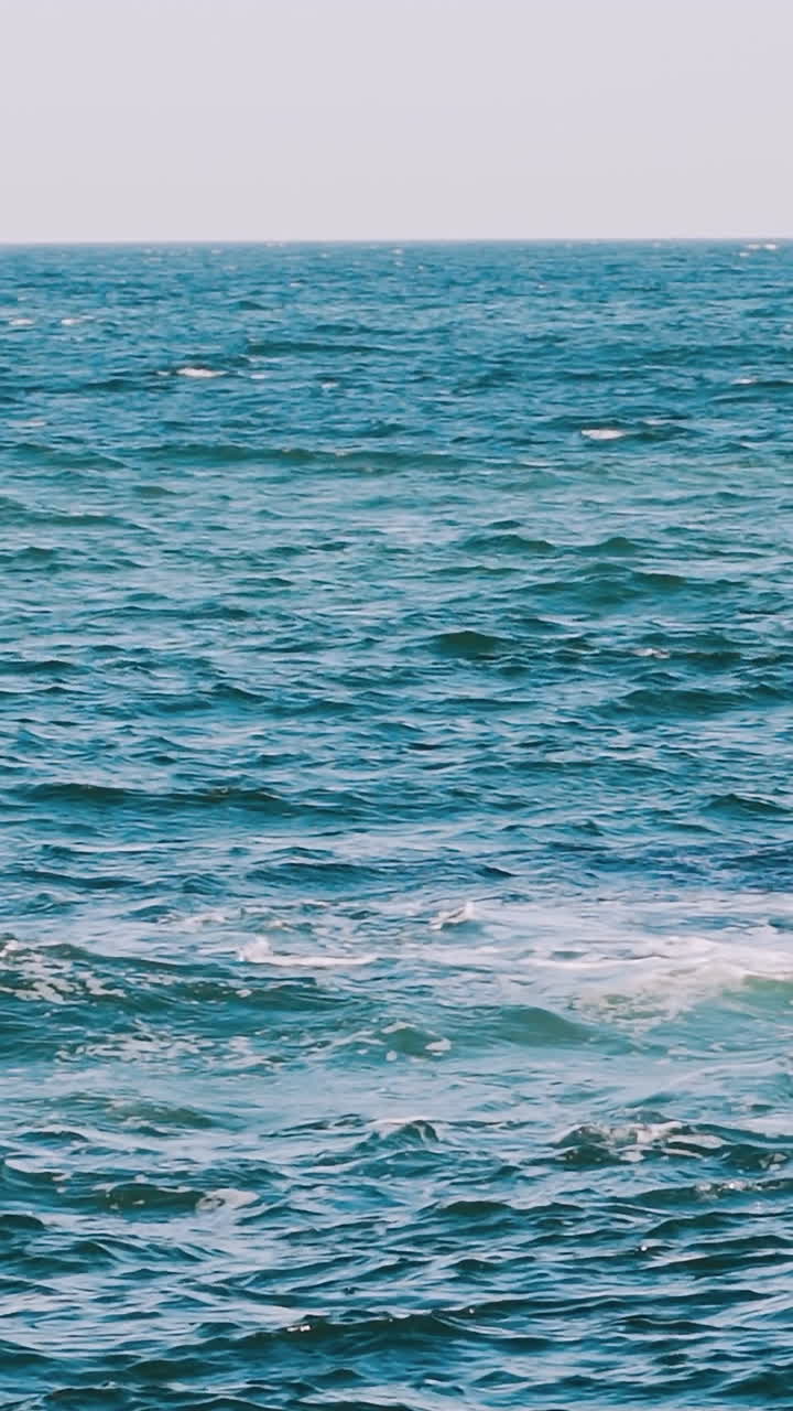 Waves swaying on the sea water. Amazing water background at storm. Beautiful blue water of the ocean with waves and white foam. Slow motion. Vertical video