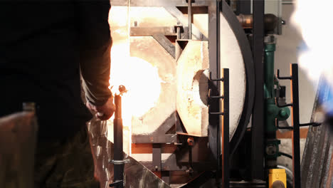 glassblower heating a piece of glass in furnace