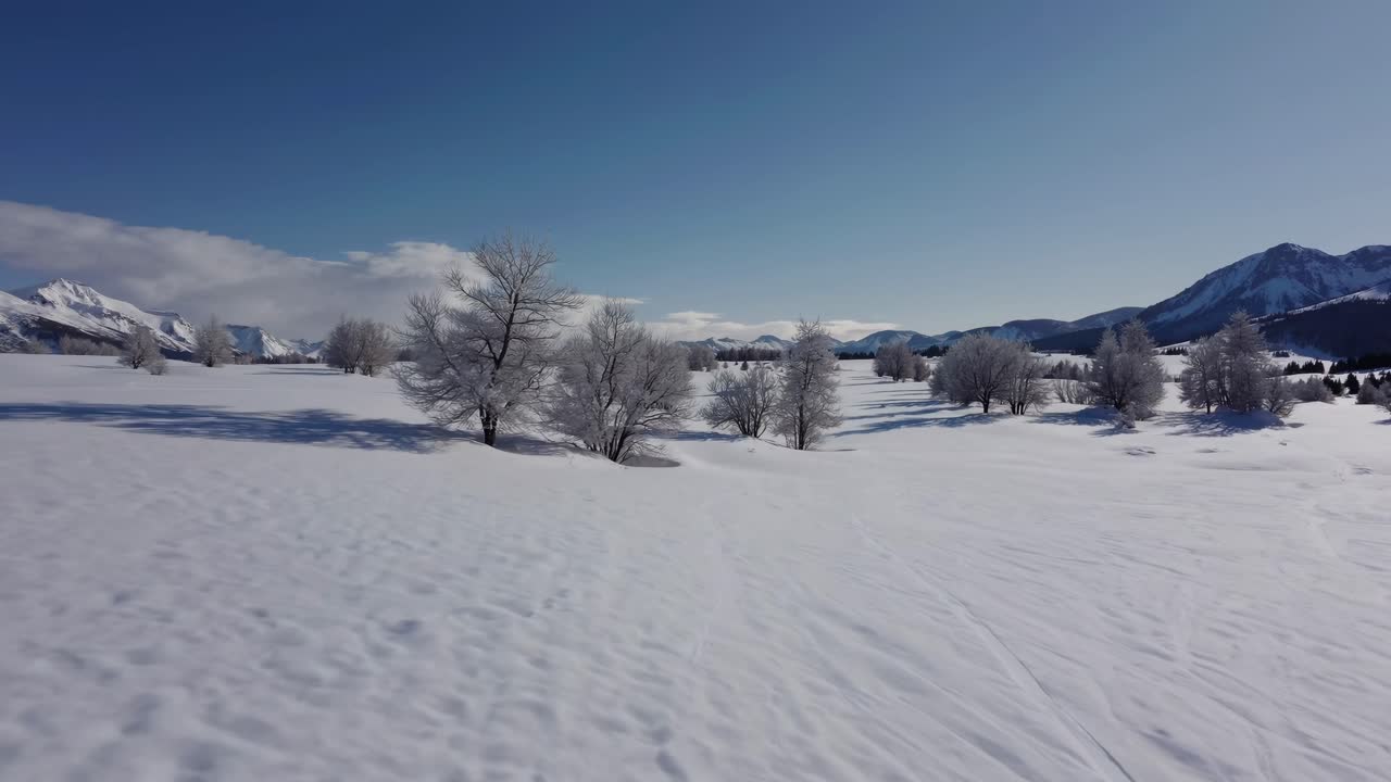 Aerial video captures a vast snowy landscape with distant mountains under a clear blue sky