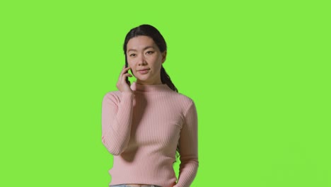 studio shot of woman answering mobile phone against green screen