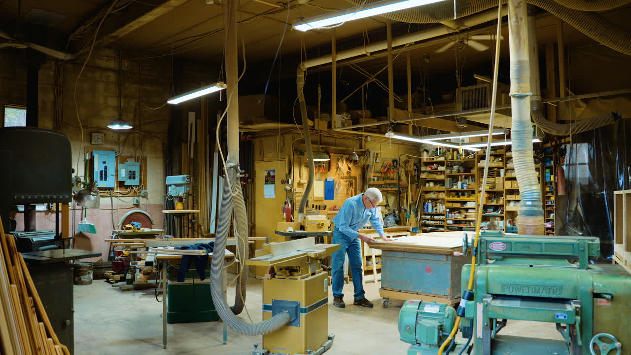 Middle-aged woodworker whittles wood in his workshop, wide shot