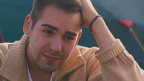 frustrated guy sits holding hand on head against blue tent