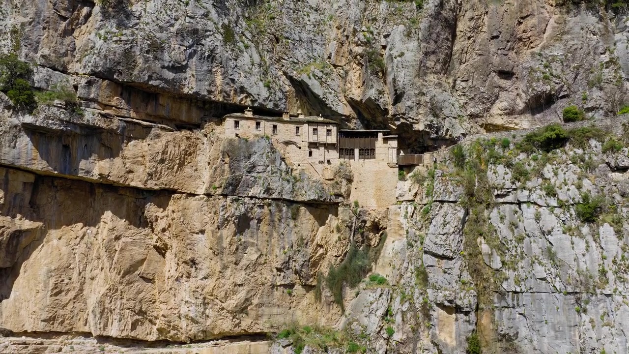 Vista aérea cercana del Santo Monasterio de Kipinas excavado en acantilados en Epiro, Grecia, con el dron descendiendo e inclinándose hacia arriba.