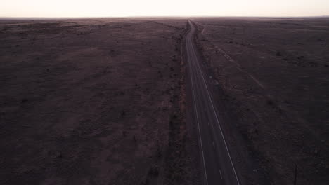 A-remote-desert-highway-with-no-cars-on-it-at-sunset,-aerial-drone