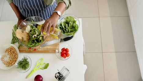 Mujer-Mayor-Afroamericana-Preparando-Ensalada-En-Una-Cocina-Soleada,-Cámara-Lenta