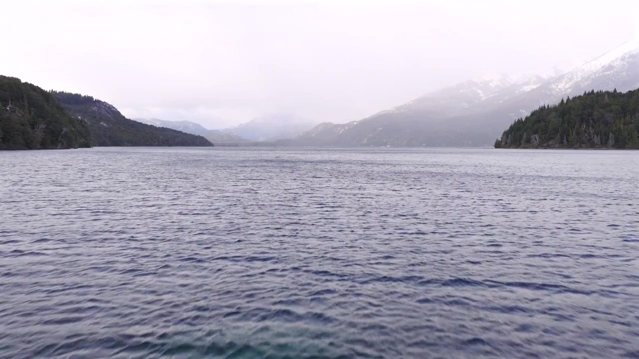 Un ponte attraversa le acque tranquille del Lago Perito Moreno, incorniciato da montagne distanti e vegetazione lussureggiante. Adatto per documentari ambientali o servizi di viaggio.