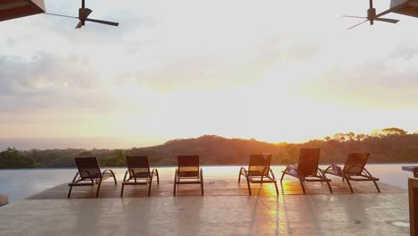 smooth tracking shot of luxury villa infinity pool and row of deck chairs during sunset