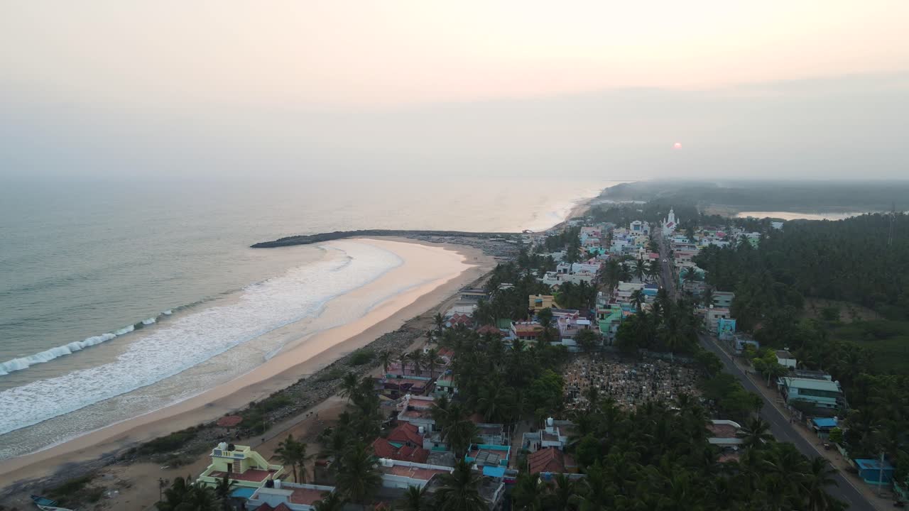 tomada panorámica aérea de drones de las olas del océano de kanyakumari que se encuentran con la ciudad bajo una puesta de sol ardiente.