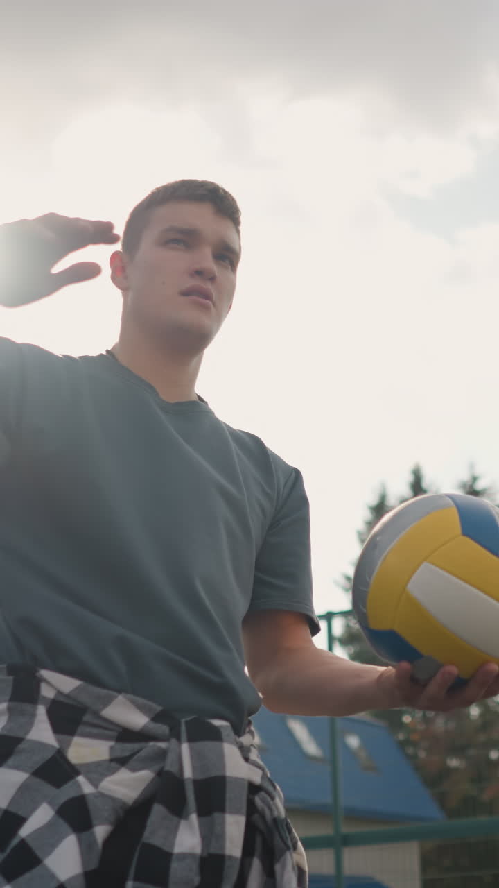 hombre rebotando la pelota de voleibol al aire libre con su mano derecha, la luz del sol creando un efecto de silueta alrededor de su hombro y cabeza, con un fondo borroso de arena deportiva y árboles