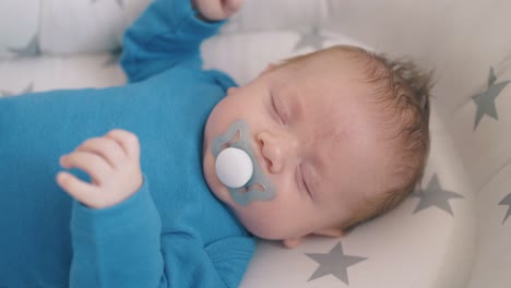 newborn-baby-waves-hands-sleeping-in-cocoon-at-home-closeup