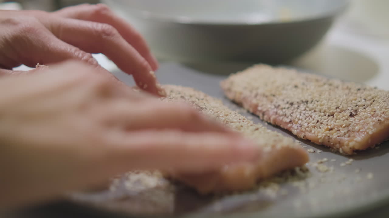 요리하기 전에 접시에 흰 양귀비 씨를 넣은 생 연어를 손으로 코팅하는 여성의 손