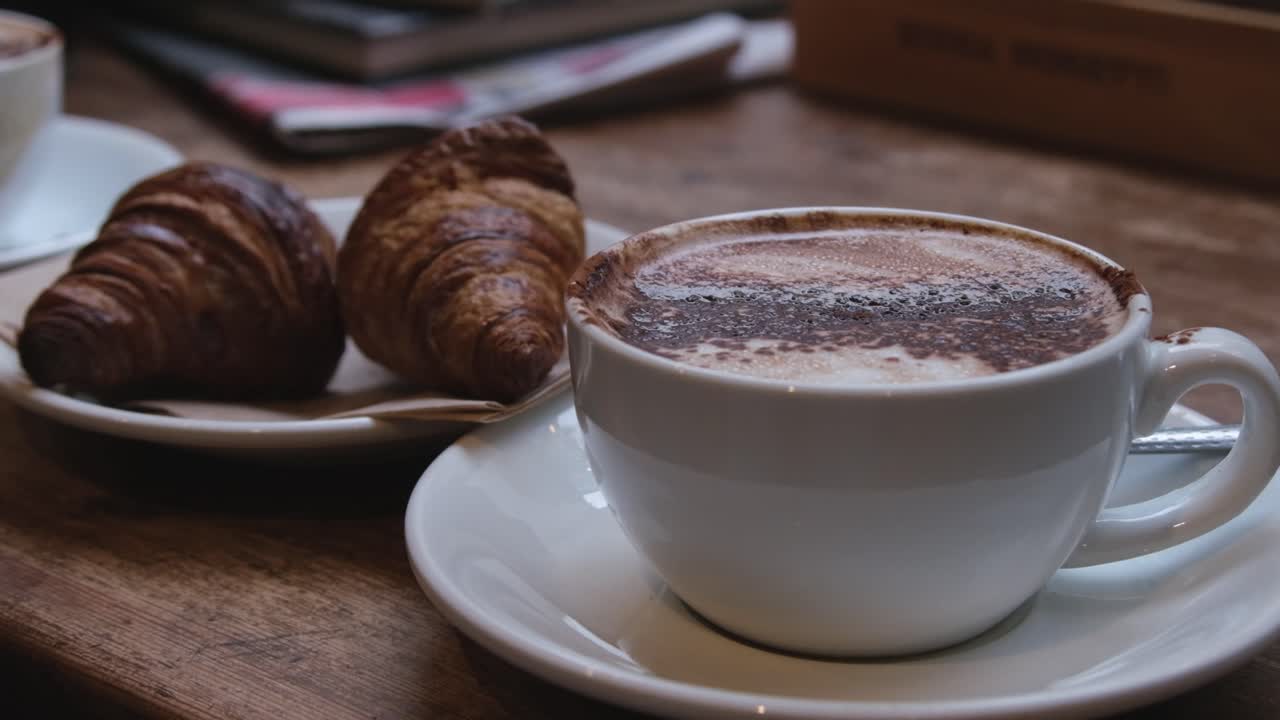 acogedora mesa de la cafetería de la mañana con dos croissants y mochaccino en una taza blanca