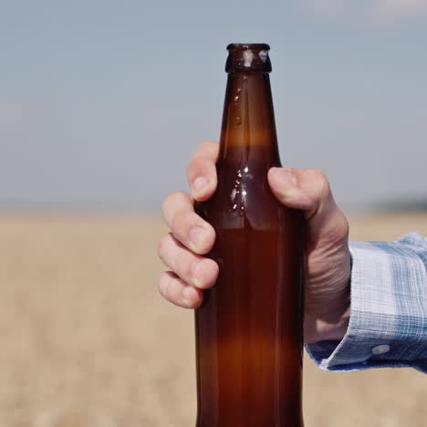 man opens a bottle of beer with wheat field in the background