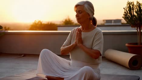 senior woman meditating on rooftop at sunset