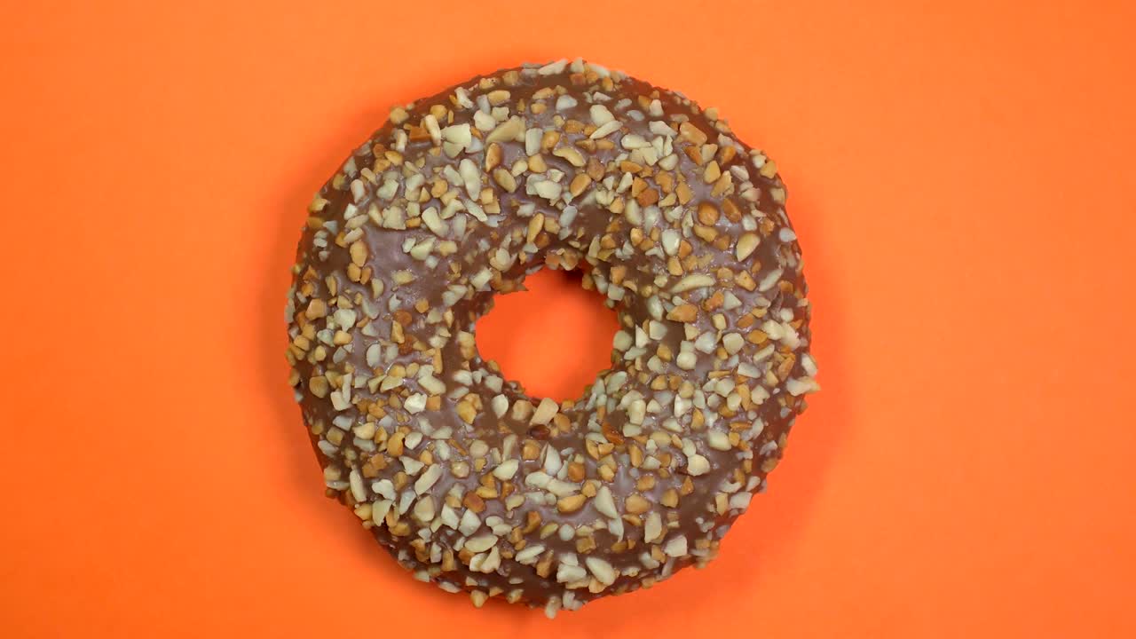 rosquilla de chocolate brillante y colorida con nueces de primer plano, macro disparado, girando sobre un fondo naranja.