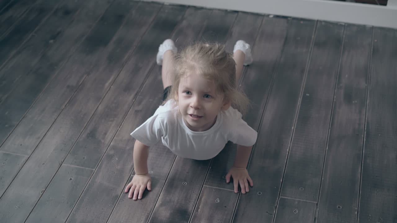 una niña linda en camiseta trata de empujar en el suelo de madera