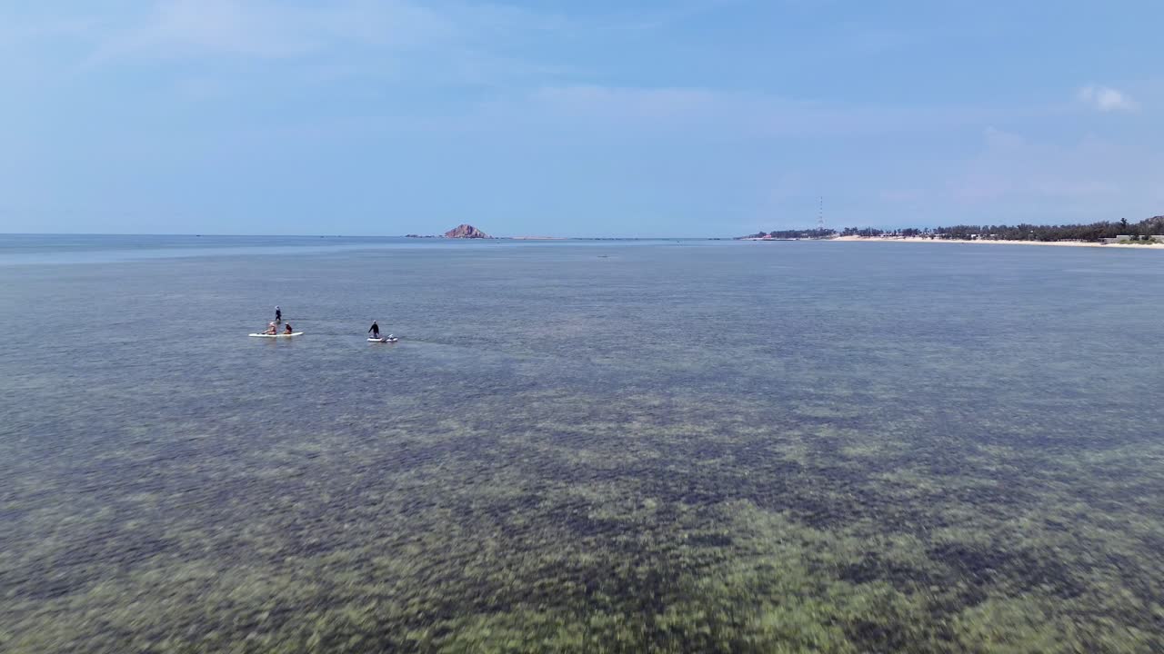 drone flies forward overflying a group of stand up paddle boarders towards the clear horizon in Vietnam