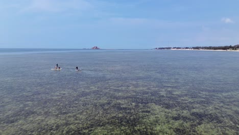drone flies forward overflying a group of stand up paddle boarders towards the clear horizon in vietnam