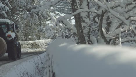 Tractor-passing-slowly-on-snowy-country-tree-lined-road-in-daytime-mid-winter