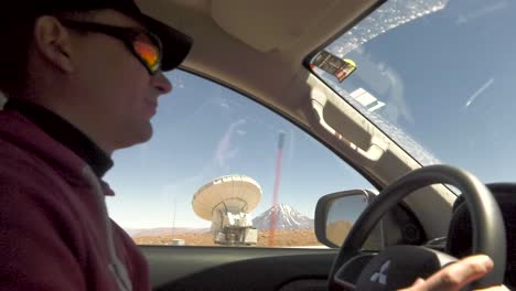 a shot of a scientist driving around the san pedro atacama desert, volcanoes in the background.