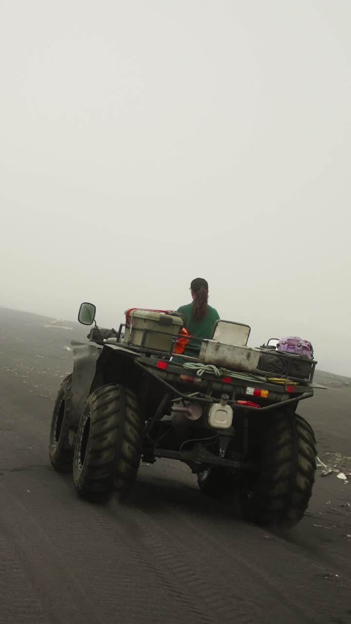 Persona che guida un ATV su una spiaggia di sabbia nera nebbiosa.