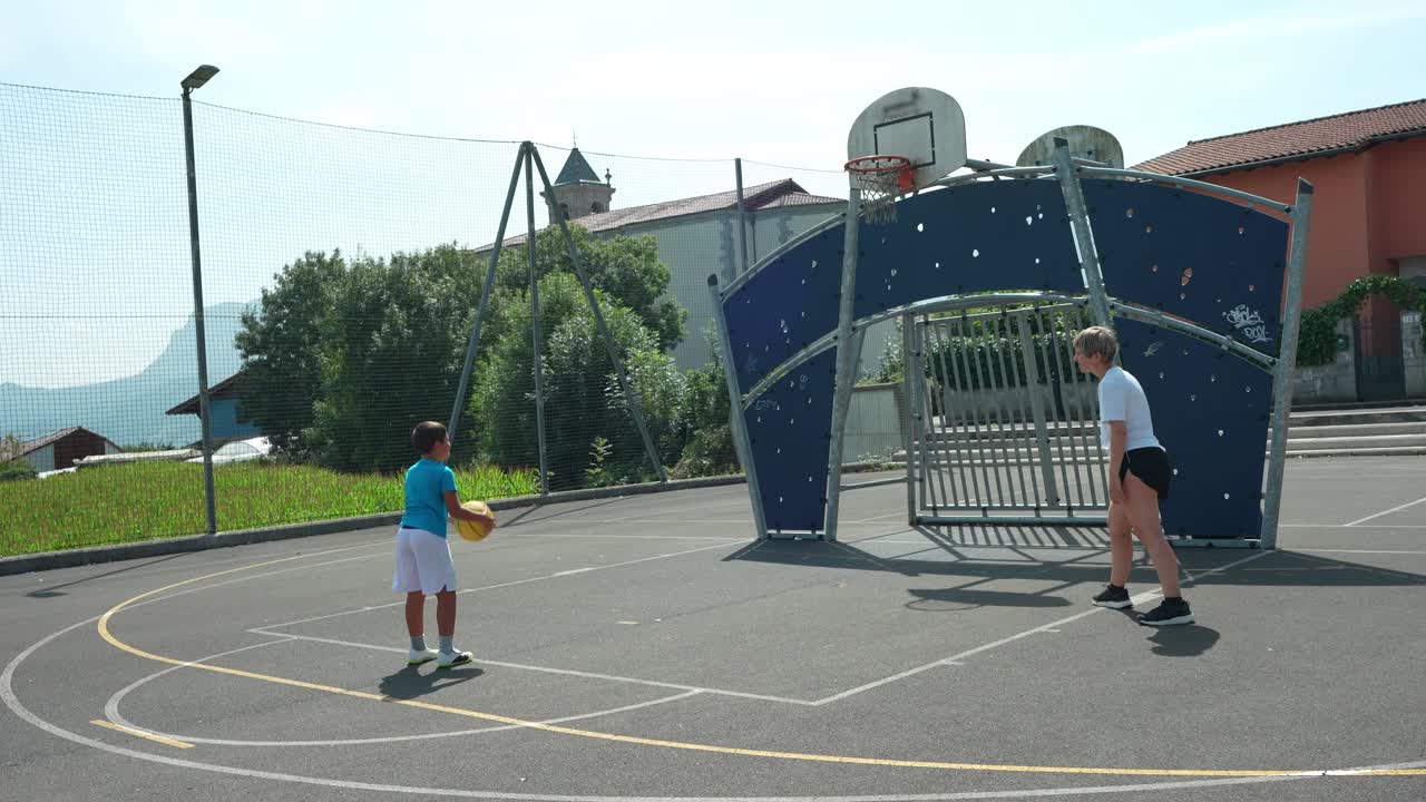 Ragazzino e donna giocano a basket su un campo all'aperto