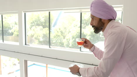 drinking tea, indian man in turban looking out window at home
