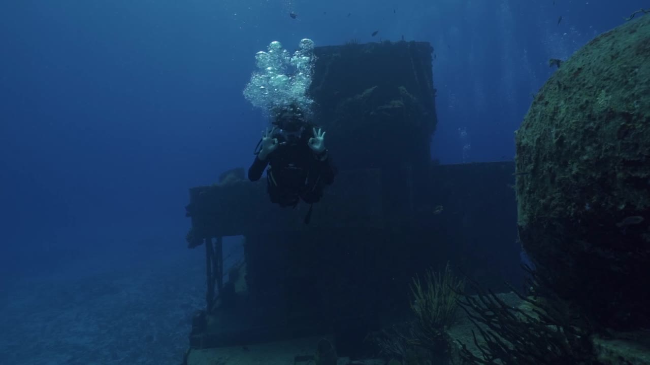A woman in full scuba gear glides past the massive hull of the ARM General Felipe Xicoténcatl (C-53), Cozumel's premier artificial reef dive site