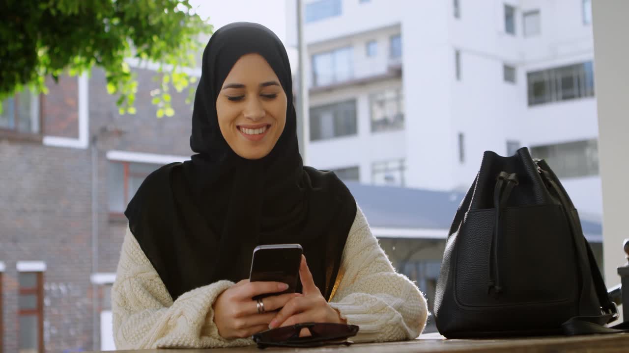 Woman in hijab using her phone in outdoor cafe 4k
