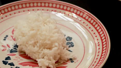 a spoon serves steamed rice onto a decorative plate. warm lighting enhances the cozy, inviting atmosphere