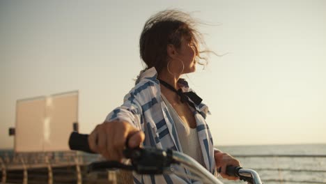 a happy brown-haired girl walks along the beach along the sea and carries her bicycle next to her. girl on a bike ride near the sea