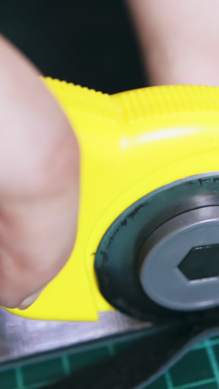 CU: Skilled tailor cuts black leather fabric with yellow rotary cutter on green cutting mat extreme close view