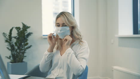 pretty young blonde business women put on face mask to work together indoors in the office