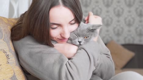 Beautiful-girl-is-sitting-in-her-room,-holding-a-grey-cat-on-her-hands-and-smiling